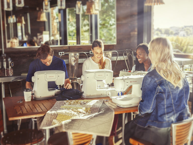 Four young adults socialising while each using their Singer sewing machines