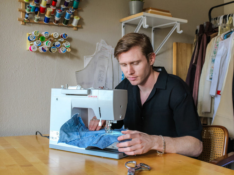 A man in a black shirt sews blue denim using a Singer Heavy Duty sewing machine
