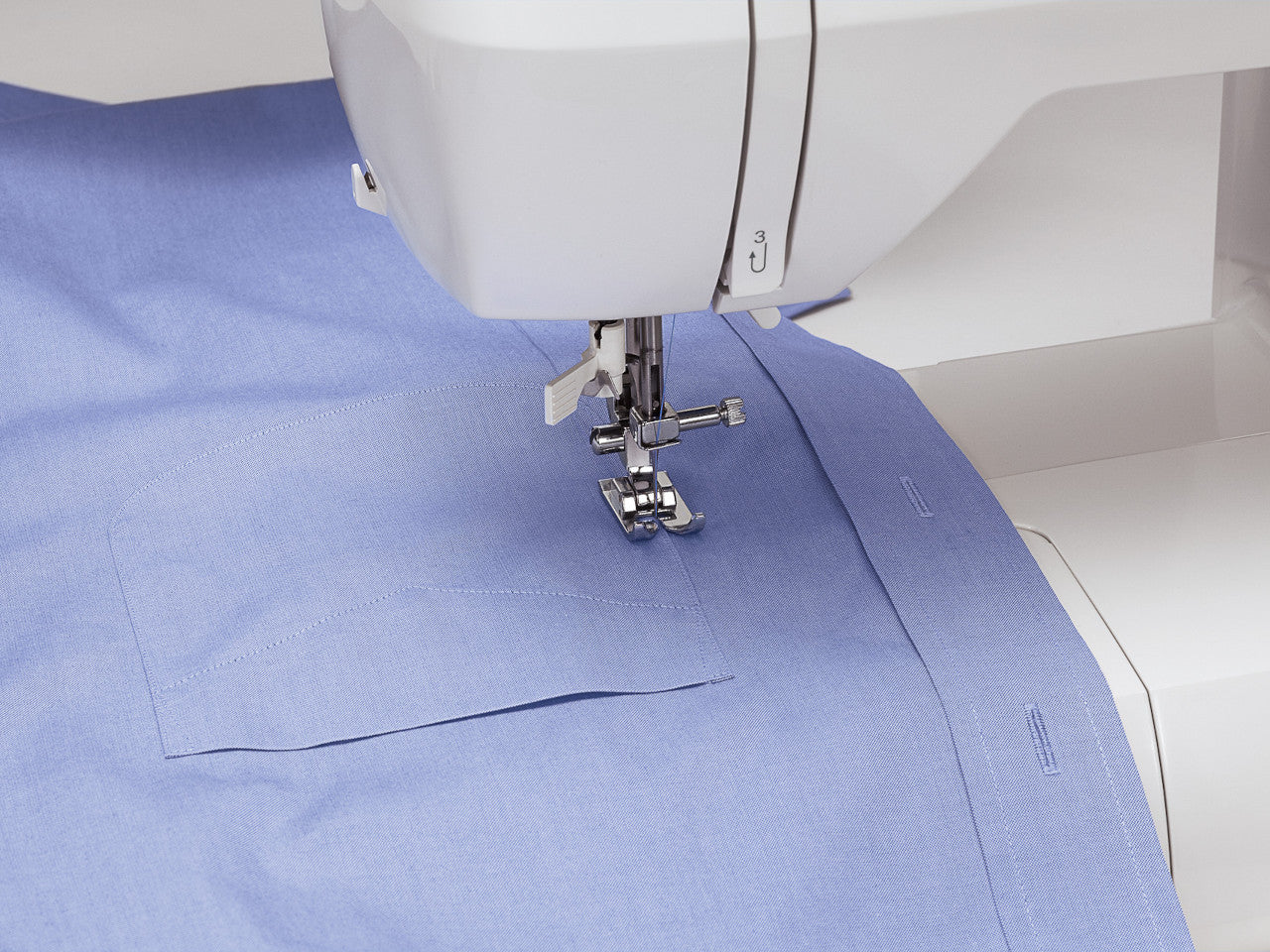 A pocket being stitched on a blue shirt with a Singer Brilliance 6199 electronic sewing machine showing the needle position