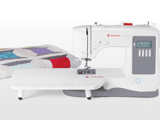 Front view of the Singer Confidence 7640 sewing machine with extension table fitted and a quilted fabric in the background.