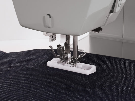 Close up of a Singer HD4411 sewing machine presser foot stitching a button hole on dark blue denim fabric.