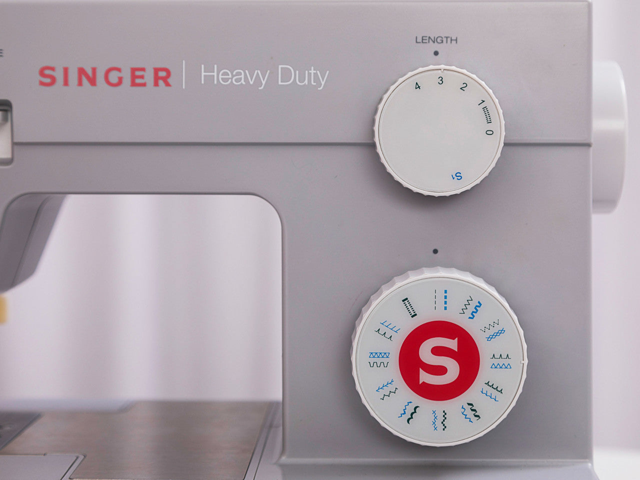 Close up of the right side of a grey SINGER HD 4423 showing the stitch type and the stitch length dials and the brand logo.