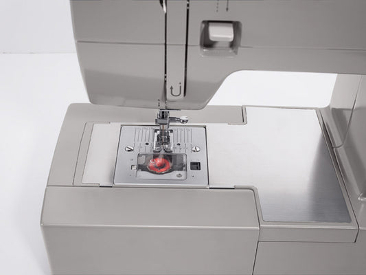 Close up of a top-drop bobbin on a SINGER heavy duty 4423 sewing machine with red thread on the bobbin.