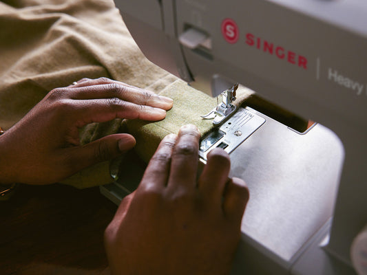 Close up of hands feeding a garment through the SINGER HD4432 heavy duty sewing machine while sewing