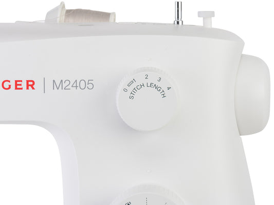 Close up of the top right corner of a SINGER M2405 sewing machine displaying the dial to adjust stitch length. A cream coloured thread spool is fitted to the top of the machine.