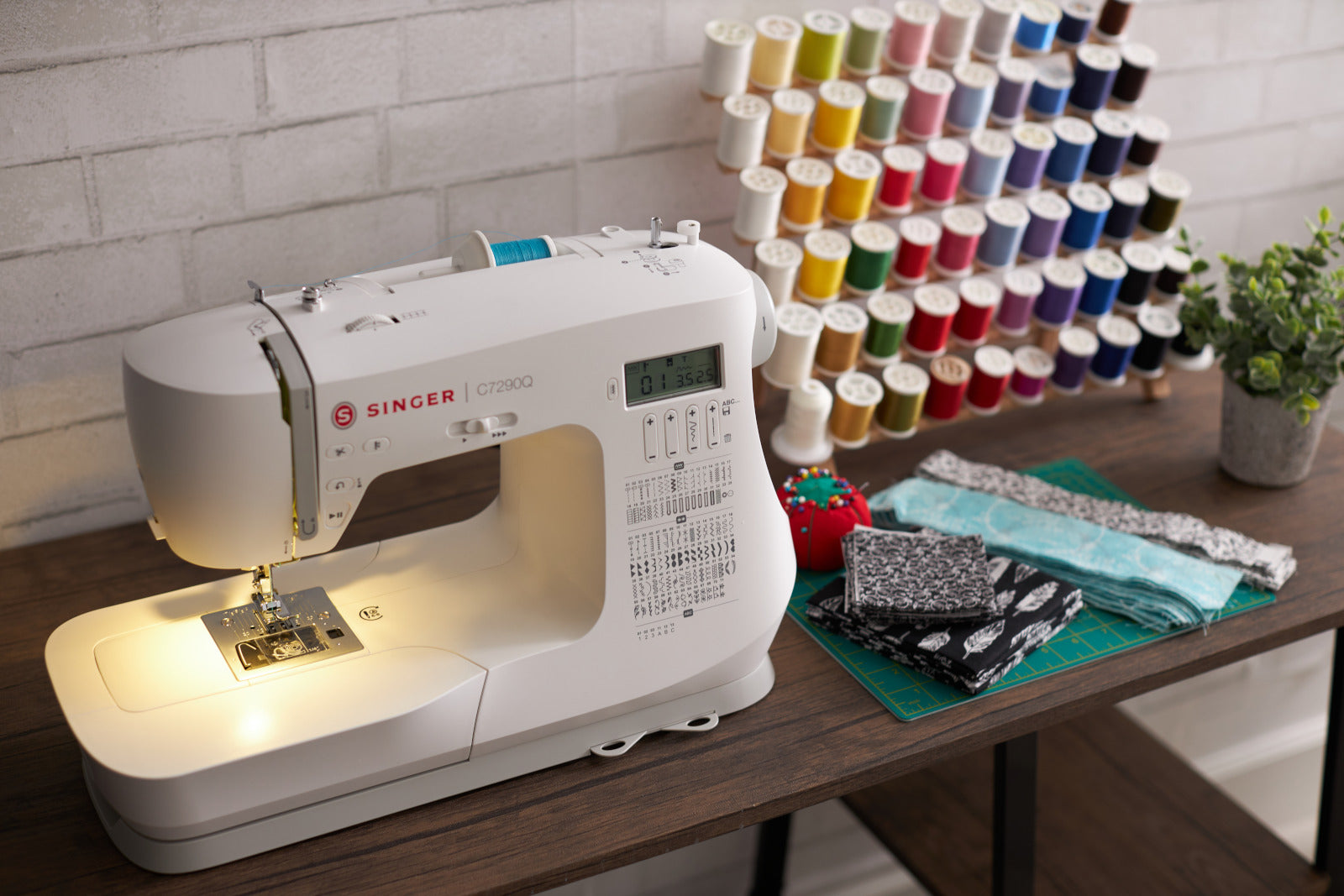 A Singer sewing machine on a wooden table with a spectrum of coloured thread mounted on the wall behind.
