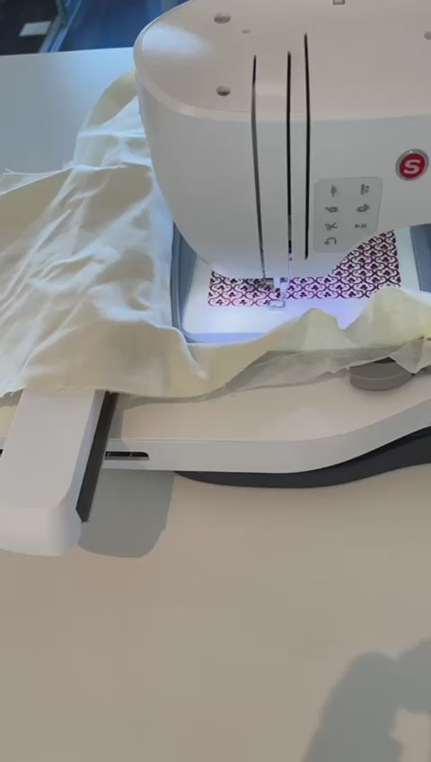 SINGER Legacy SE300 sewing and embroidery machine embroidering an intricate red floral pattern onto a piece of white fabric clamped in an embroidery hoop.