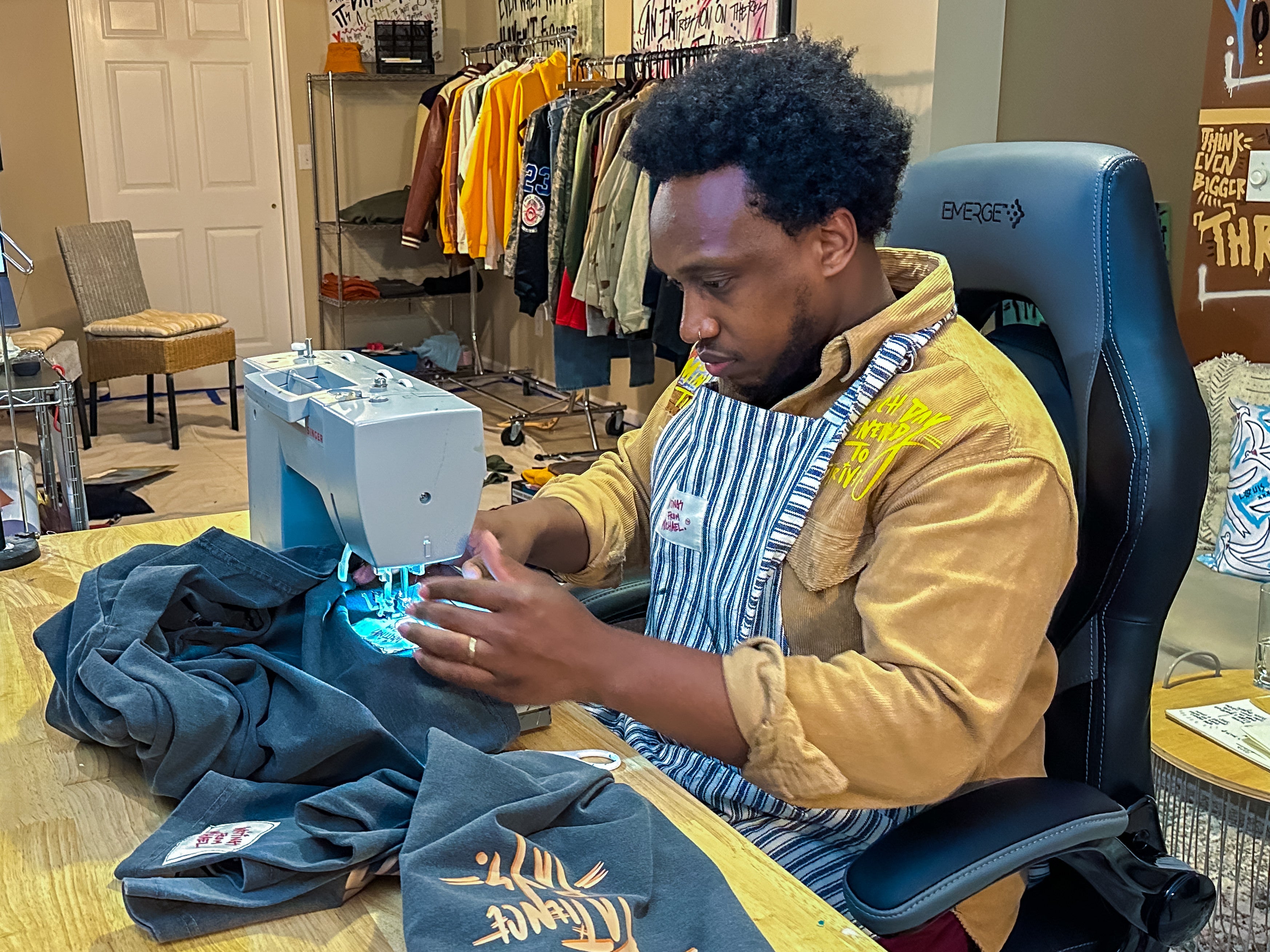 A man concentrates while stitching heavy duty fabric using a Singer heavy duty sewing machine in a sewing room.